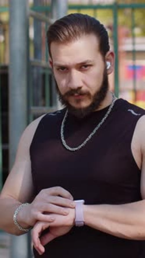 Athletic Lebanese Man in Sportswear Using Smart Watch Listening Music on Earphones on Playground