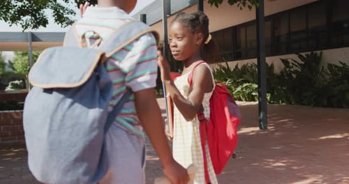 Video of happy african american boy and girl with schoolbags high fiving outside school