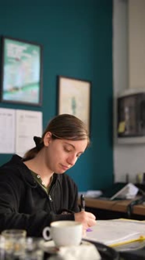 A Woman is Fully Concentrated on Studying at a Cafe Showing Dedication to Her Academic Goals