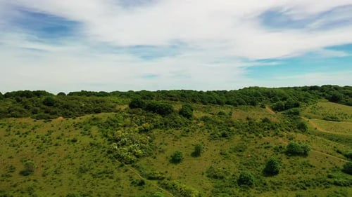 Foto aérea subindo acima de uma encosta em uma paisagem rural, em um dia ensolarado.