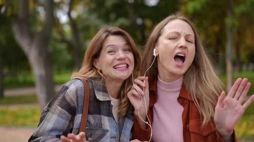 Portrait of Two Joyful Women Singing Grimacing Looking at Camera Enjoying Hobby in Autumn Park