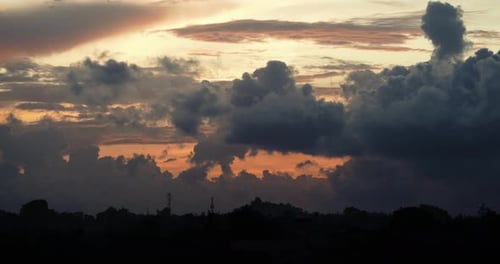 Dark clouds pass over yellow orange sunset. Time Lapse