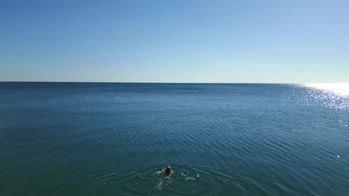 Jovem mulher começa a nadar para o mar, a câmera a segue por trás