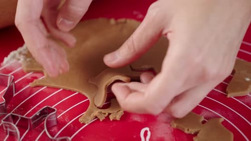 Hands Cutting Gingerbread Dough on Red Mat