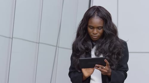 Woman smiles while using tablet in front of building