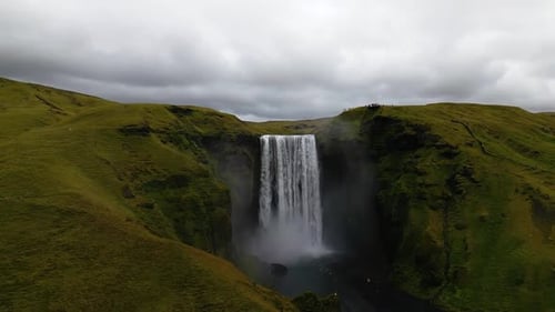 cinematic drone footage of Skógafoss Waterfall in Iceland, capturing the immense curtain of water