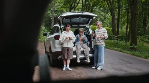 Family Having Hot Tea by Open Car Trunk while Standing on Country Road