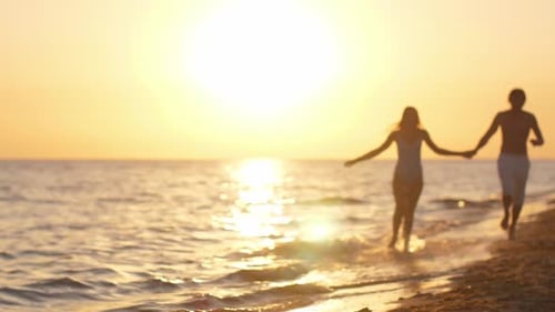 Happy Couple in Love Holding Hands and Running on Beach at Sunset
