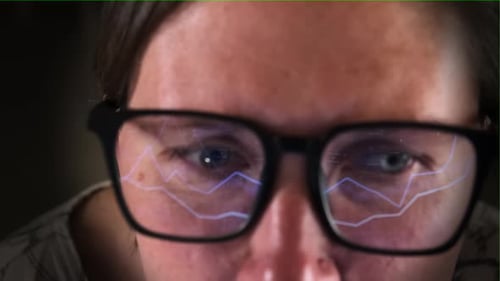 Eine Frau im Online-Handels-Börsendatendiagramm im Amt mit Lichtreflexion auf der Brille