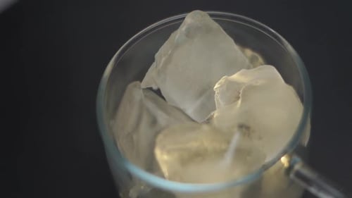The coffee is falling into transparent glass cup full of ice