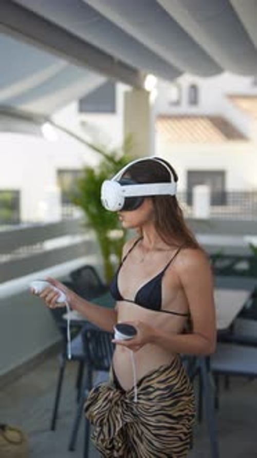 A Woman is Enjoying a Virtual Reality Experience Outdoors While Wearing Swimwear on a Terrace