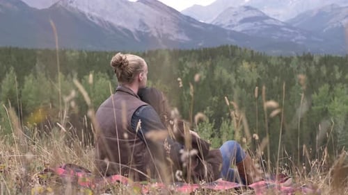Young couple enjoying romantic mountain getaway hugging on blanket in woods
