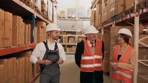 Handsome man in work uniform conducts a tour of the warehouse with boxes for an elderly man and a yo