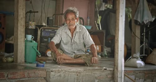 Elderly Man Smiling, Sitting Cross-Legged on Floor Indoors