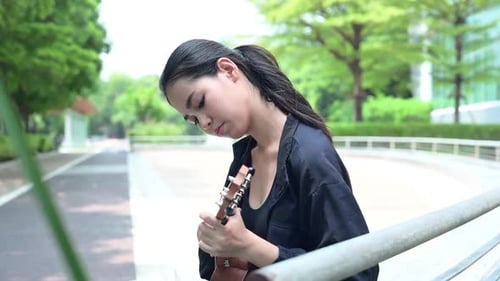 Teenage girl with holiday activities, Playing the ukulele in the park