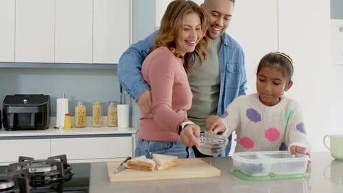 Contenant d'emballage familial diversifié pour fille dans la cuisine tranchant un sandwich en ajoutant des myrtilles et du jus