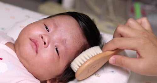 Infant Having Hair Brushed in Bed