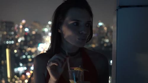 Elegant woman sipping cocktail on rooftop terrace at night contemplating life