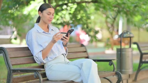 Woman Using Phone and Credit Card on Bench
