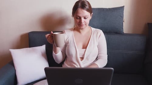 Woman Using Laptop and Drinking Coffee at Home