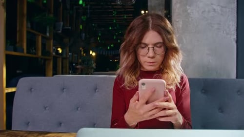 Happy Young Woman Sits with Phone and Computer at the Table