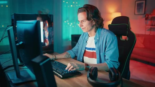 Excited Gamer Playing Online Video Game on His Personal Computer. Room and PC have Colorful Warm Ne