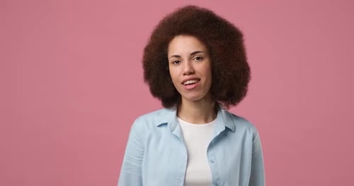Smiling Attractive African American Woman Winks Looking at Camera Standing Over Pink Studio