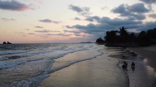 Aerial: Kids silhouettes playing on the ocean beach at a beautiful sunset. Tropical islands on the b