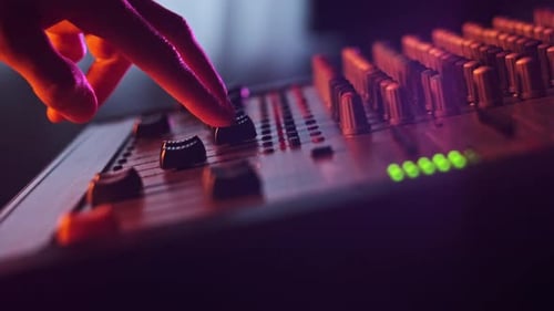 Sound Engineer Moves Faders Up and Down on Audio Mixer in Neon Light CloseUp