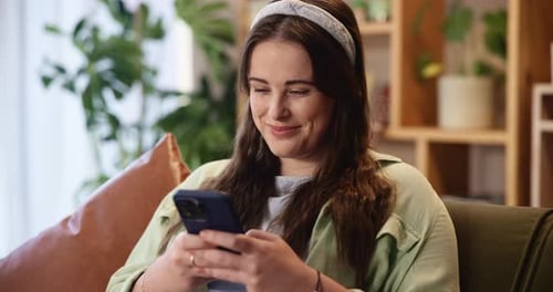Woman Smiling and Using Mobile Phone on Sofa