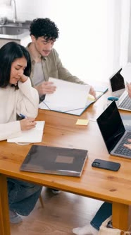 Young Adults Work Together at Table on Laptops