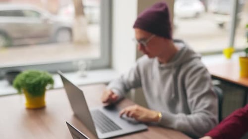Two Hipster Coworkers Sharing Ideas About Project Sitting with Laptops in Spacious Open Space Office