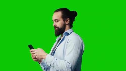 Young Carefree Man Checking His Mobile Phone Against Green Screen Backdrop