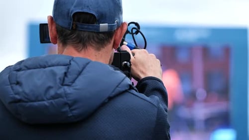 Professional Cameraman Filming Event Outdoors Capturing Footage with Handheld Video Camera