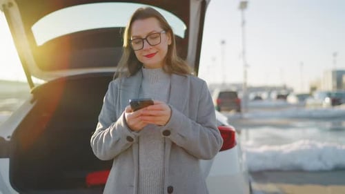 Woman Using Phone Near Open Hatchback of Car