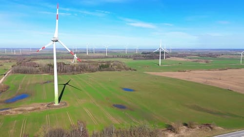 Aerial footage of wind turbines in a wind farm generating green electric energy on a wide green fiel