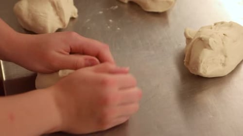 Baker's Hands Kneading Bread Dough On Stainless Tabletop In The Kitchen - close up