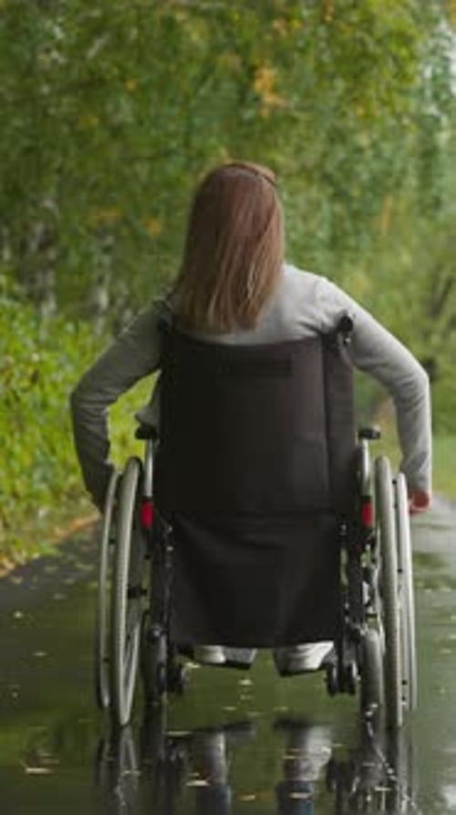 Young Woman in Wheelchair After Injury Walks in Park in Rain