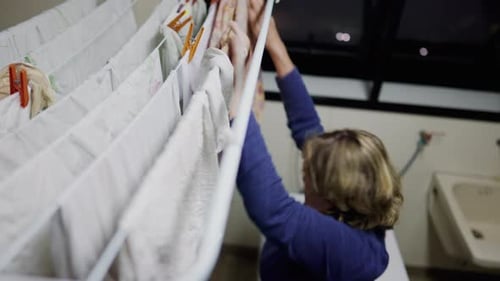 One senior woman putting clothes to dry seen from above. An older lady drying sheets on rack