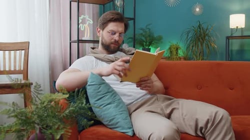 Young Adult Reading a Book on Couch at Home