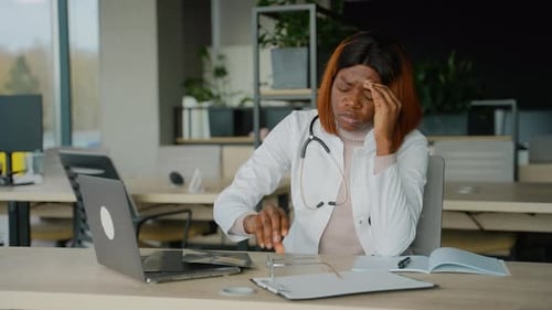 Stressed Woman Doctor Massaging Head at Desk