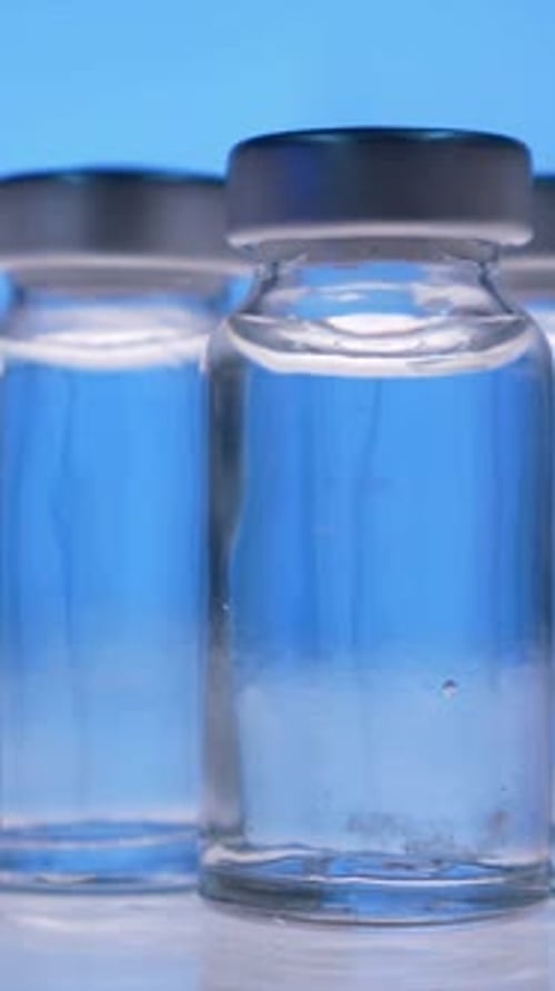 Three Vaccine Vials with Clear Liquid on Blue