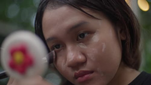 Young Woman Applying Makeup with Brush and Mirror