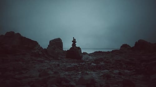 Sunset Silhouette of a Person Balancing Rocks on a Calm Shore
