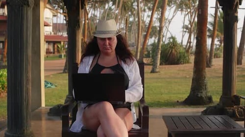 Seriöse Freelancerin arbeitet online am Laptop und sitzt in der Nähe eines Hotels in den Tropen