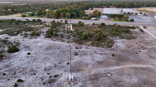 Aerial top shot of a single telecommunication tower standing tall beside a running highway at countr