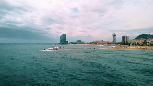 Aerial view over the sea on the coast of the Barceloneta Beach, towards the Hotel W, cloudy day, in