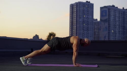 Muscular Man Doing Push-ups on Rooftop at Sunrise