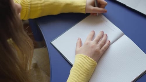 Person Writing in a Notebook on a Blue Desk Wearing a Yellow Sweater The Notebook is Open with Graph