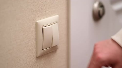 A mão de uma mulher acende a luz com um interruptor elétrico, de perto